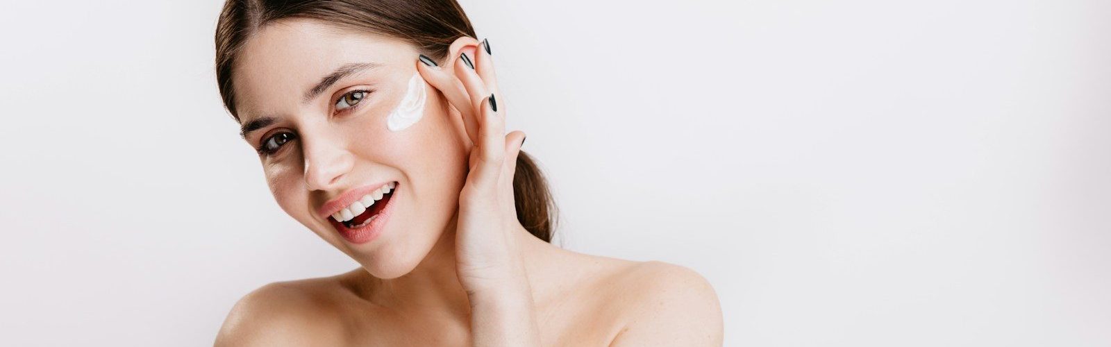 A woman in a white shirt is smiling and touching her face