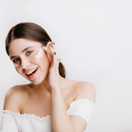 A woman in a white shirt is smiling and touching her face